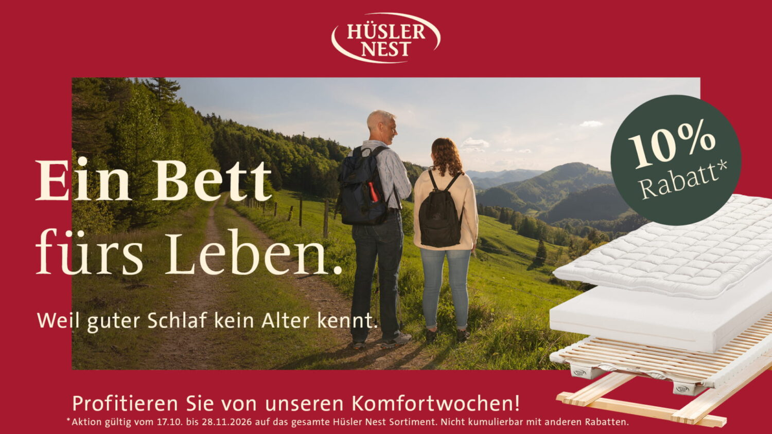 Hüsler Nest Herbstaktion - Ein Bett fürs Leben. Weil guter Schlaf kein Alter kennt. Profitieren Sie von unseren Komfortwochen! 10% Rabatt. Aktion gültig vom 17.10. bis 28.11.2026 auf das gesamte Hüsler Nest Sortiment. Nicht kombinierbar mit anderen Rabatten. Ein Mann und eine Frau stehen auf einem Wanderweg vor einem Bergpanorama. Daneben ist ein Bettaufbau mit Gestell, Lattenrost, Matratze und Auflage zu sehen.